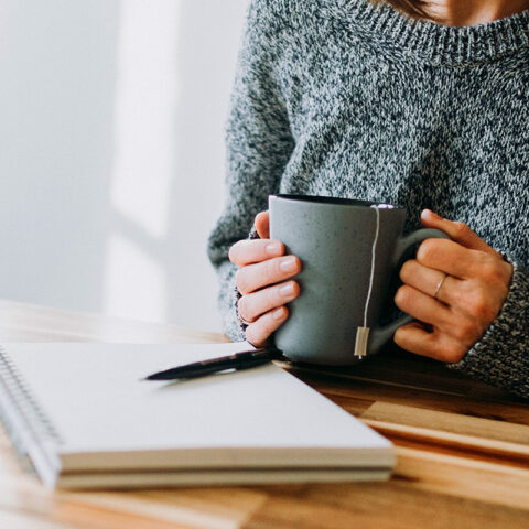 A wooman business owner holding a mug of hot tea as she stares at a blank page, unsure of what to write about for her next business blog post